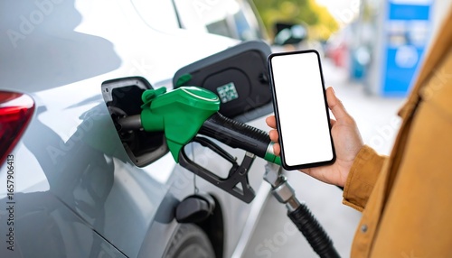 Person holding smartphone with blank screen near car fuel nozzle at gas station.