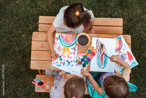 Billede på lærred Children painting with watercolors at a wooden table in a garden
