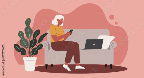 Senior woman comfortably using a smartphone on her sofa at home, with a laptop nearby. Depicts modern digital lifestyle and connectivity.