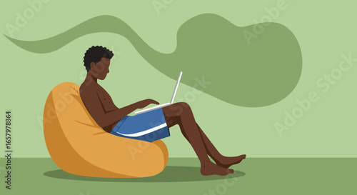 Young man in swim shorts sits on a bean bag, working on a laptop in a relaxed setting. Ideal for remote work, summer, or digital lifestyle concepts.
