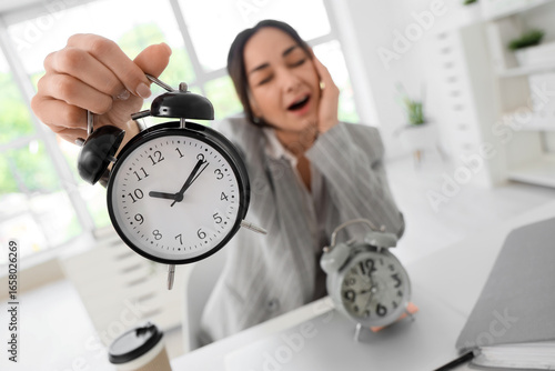 Tired businesswoman with alarm clock in office, closeup. Time management concept