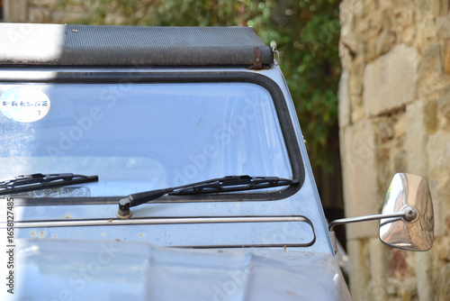 Closeup of vintage Citroën 2CV windshield and mirror parked by rustic stone wall, retro detail highlighting timeless French automotive design and nostalgic travel lifestyle.