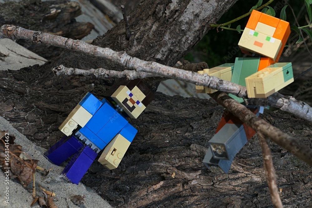 Fototapeta premium LEGO Minecraft large figures of Steve and Alex climbing on dried fallen broadleaf tree branches on sandy bank of Danube river, southern Slovakia.