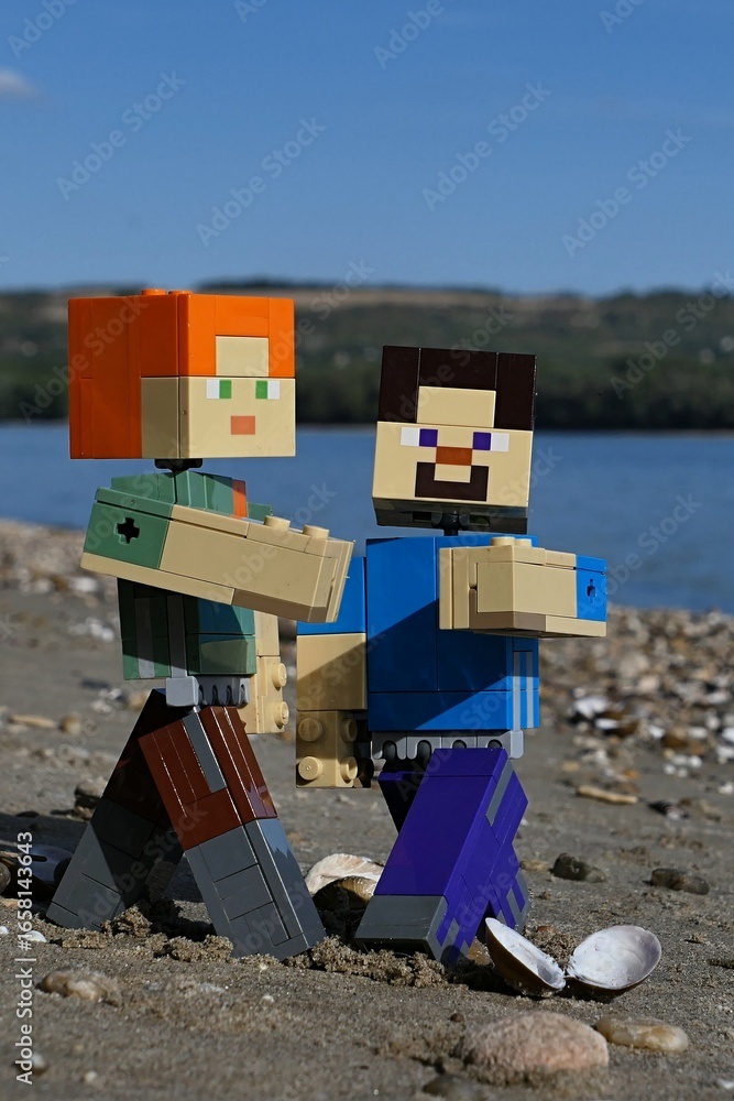 Obraz premium LEGO Minecraft figures of Steve and Alex, dancing between clams and stones on sandy river Danube bank, borderline between Slovakia and Hungary. Forested opposite bank and blue skies visible.