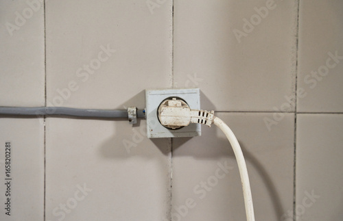 Old Electrical Outlet with Plug on a Tiled Wall

