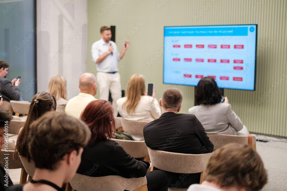 Fototapeta premium Professional speaker presents training session to audience in modern business seminar setting