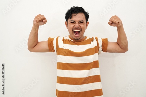 Fotografía A young Asian man in a white and brown striped shirt shows off his muscles with a happy expression