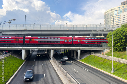Moscow, Russia - 05.31.2025: Aeroexpress train from Sheremetyevo airport on the bridge on Kuntsevskaya metro station of Moscow central diameters. Car traffic on Rublevskoe highway.
