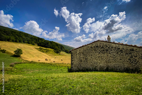 Rolling Tuscan hillside with weathered stone barn, golden hay bales bathing in warm sunlight