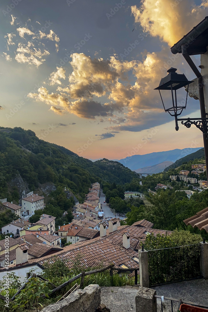 Fototapeta premium Golden sunset lighting terracotta rooftops of quaint italian hillside village, vintage lamppost framing scenic landscape