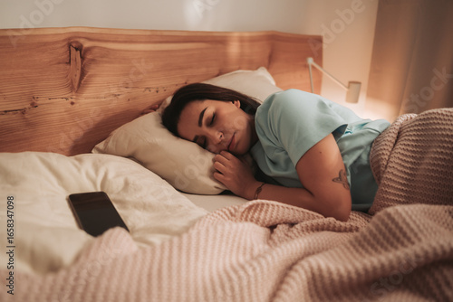 A woman sleeps peacefully in a cozy bedroom with her cell phone beside her