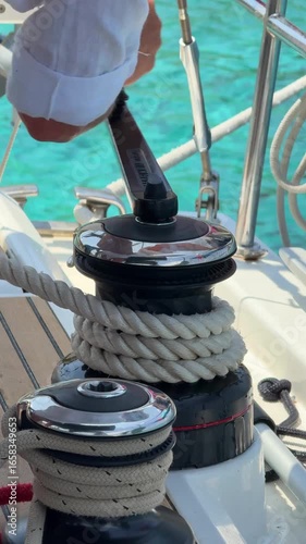 Close-up of hands tightening rope on winch during sail hoisting on sailing yacht. Teamwork and manual control in recreational boating activity.