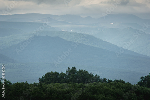 Fotografía Serene landscape featuring layered mountains shrouded in mist, with lush green f