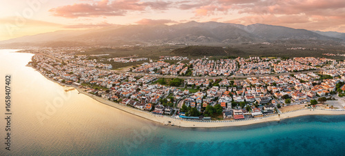 Fototapeta Naklejka Na Ścianę i Meble -  Calm sea reflecting the warm colors of sunset over the coastal town of Akcay, Turkey, with mountains in the background