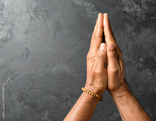 Praying Hands with Wooden Bead Bracelet on Gray Textured Background