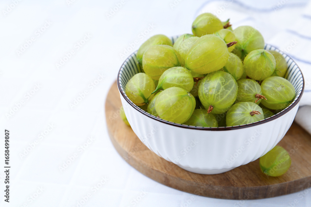 Fresh green gooseberries in bowl on white table, closeup. Space for text Fresh green gooseberries in bowl on white table, closeup. Space for text