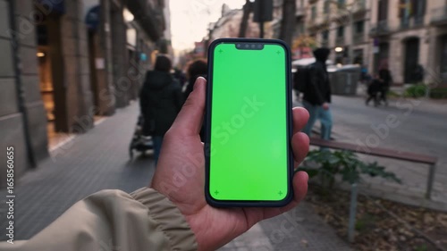 Man holds in hand smartphone with green screen mock up, using app. Urban life and leisure concept. 