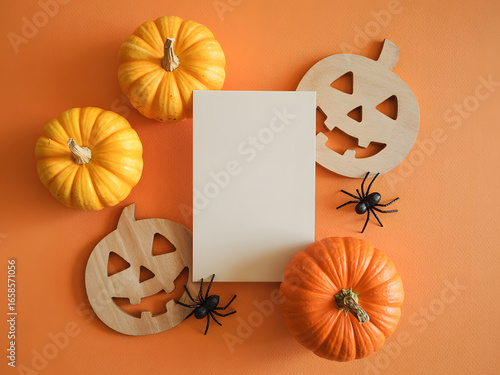 Halloween flat lay mockup with pumpkins, wooden jack o lantern decorations, black spiders and blank card on orange background, spooky autumn holiday design template for invitations and greeting cards.