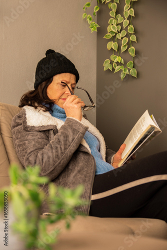 mulher de 55 anos lendo livro em casa, colocando óculos de leitura, clima de inverno