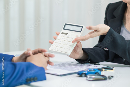 car dealership is talking with customer in their office to offer promotions and deals as they sign sales contract. contract document is laid out on table in dealership office ready for customer sign.