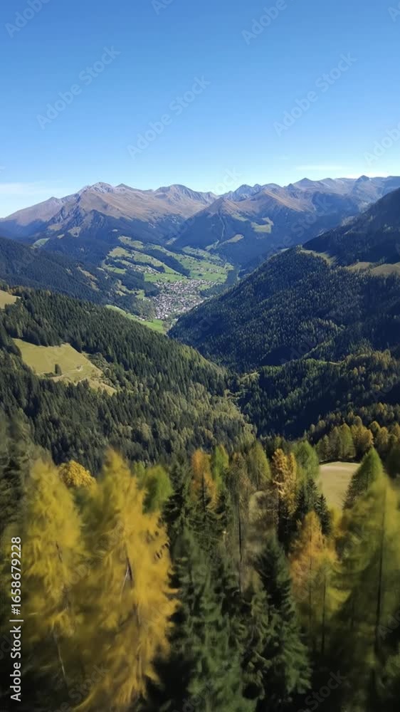 Mountain vista reveals a valley town amid forests, under a clear blue sky
