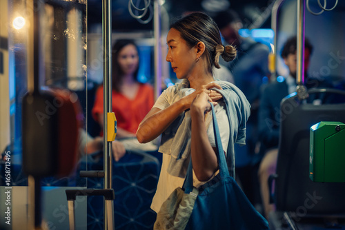 Photos Young woman standing on a bus at night holding her sweater and bag