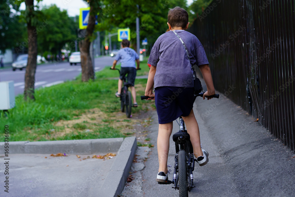 Fototapeta premium Two boys riding bicycles along a city street during the late afternoon
