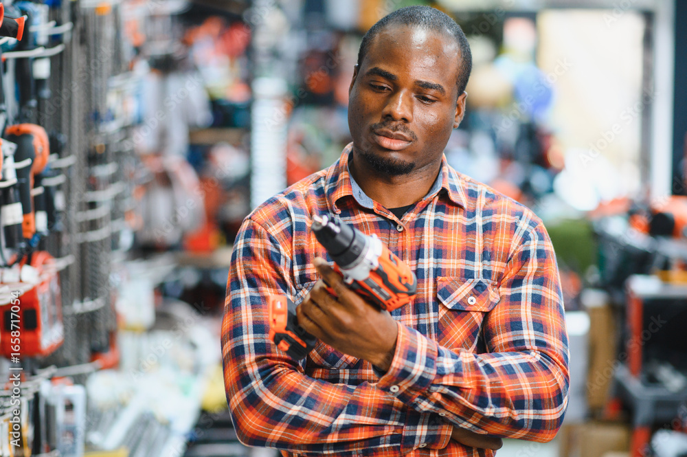 Obraz premium African americam man buying modern electric drill while standing in tool. Hardware construction site objects concept