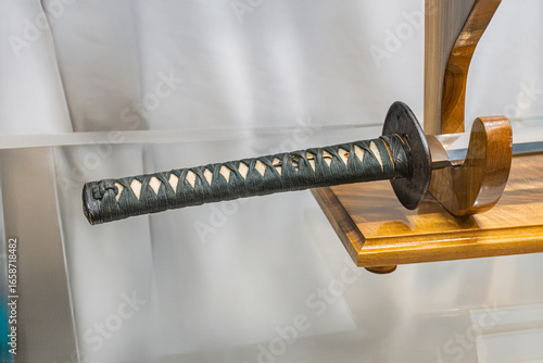 Close-up of a katana on a stand, with a ridged blade and bamboo grip, against a blurred background Even lighting without shadows or text Documentary style