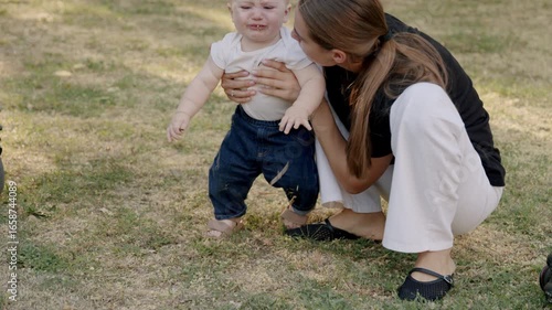 Mother comforts her baby after a fall, gently wiping away tears while embracing him in a nurturing outdoor setting, showcasing love and care in a heartfelt moment