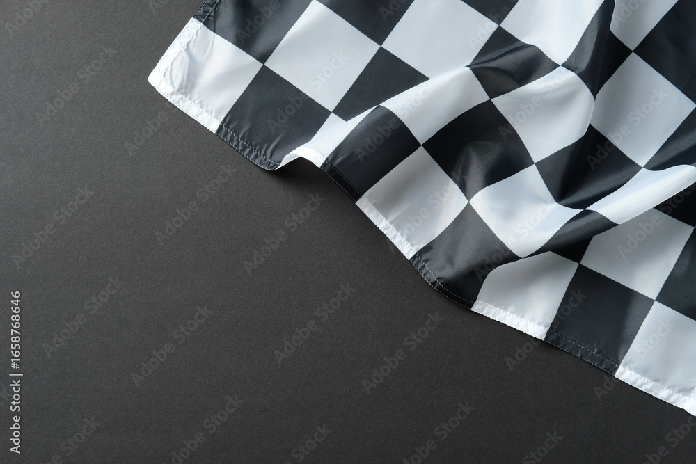 Obraz premium Checkered racing flag on dark surface, symbolizing finish line, victory, and motorsport.