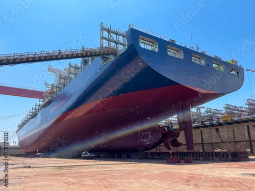 Large container ship in dry dock with stern, hull, and propeller visible during maintenance.