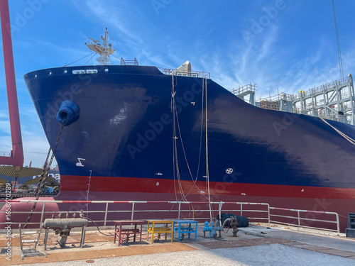 Large container vessel (bow part) docked at shipyard with crane during maintenance.