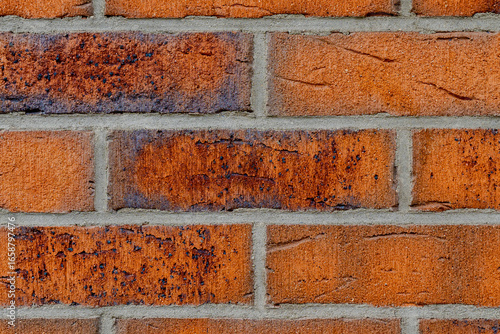 Close-up of weathered red brick wall with dark stains