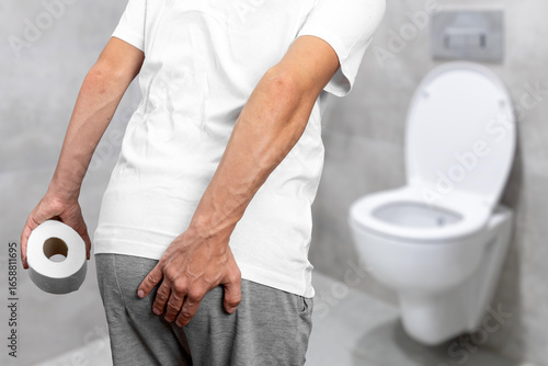Obraz na plátně Man suffering from hemorrhoids or rectal pain holding his backside in bathroom, concept of digestive health issues, constipation, anal itching, prostate problems, and urinary tract infection symptoms