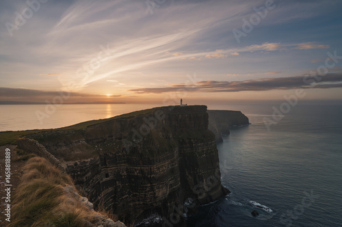 Dramatic sunset over a rugged cliff overlooking the vast ocean, creating a scenic landscape.