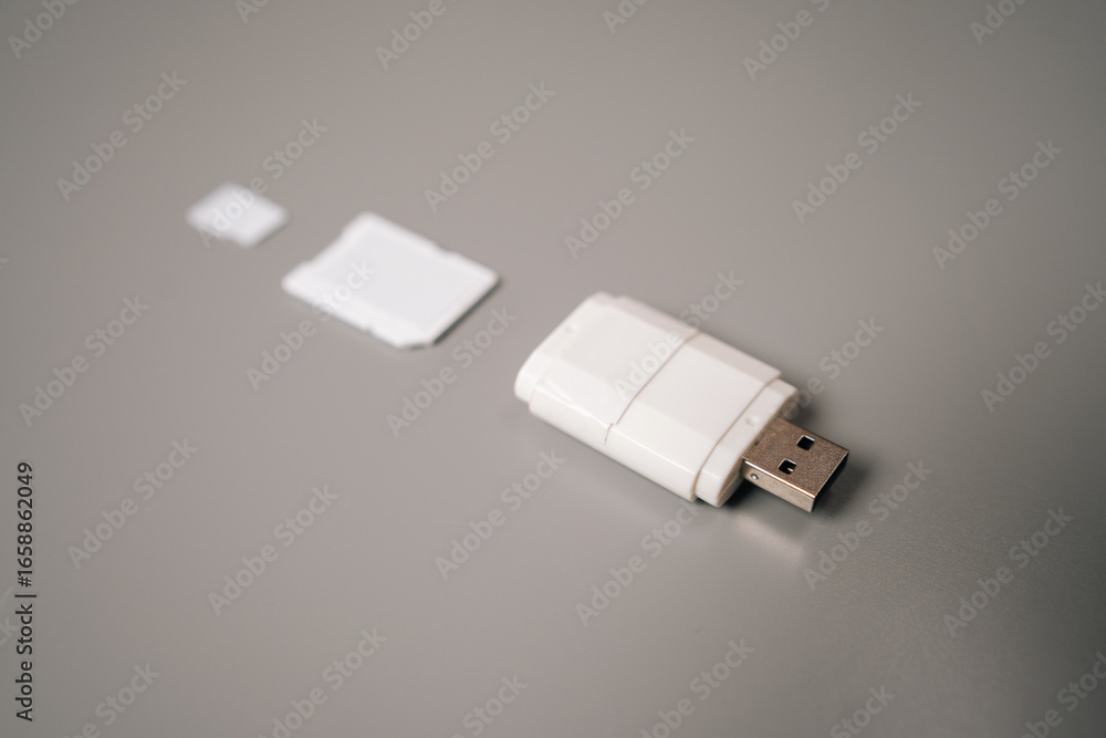 Fototapeta premium Close-up of white micro sd card reader featuring usb connector resting on gray table, accompanied by adapter and microSD card, highlighting compact and portable design