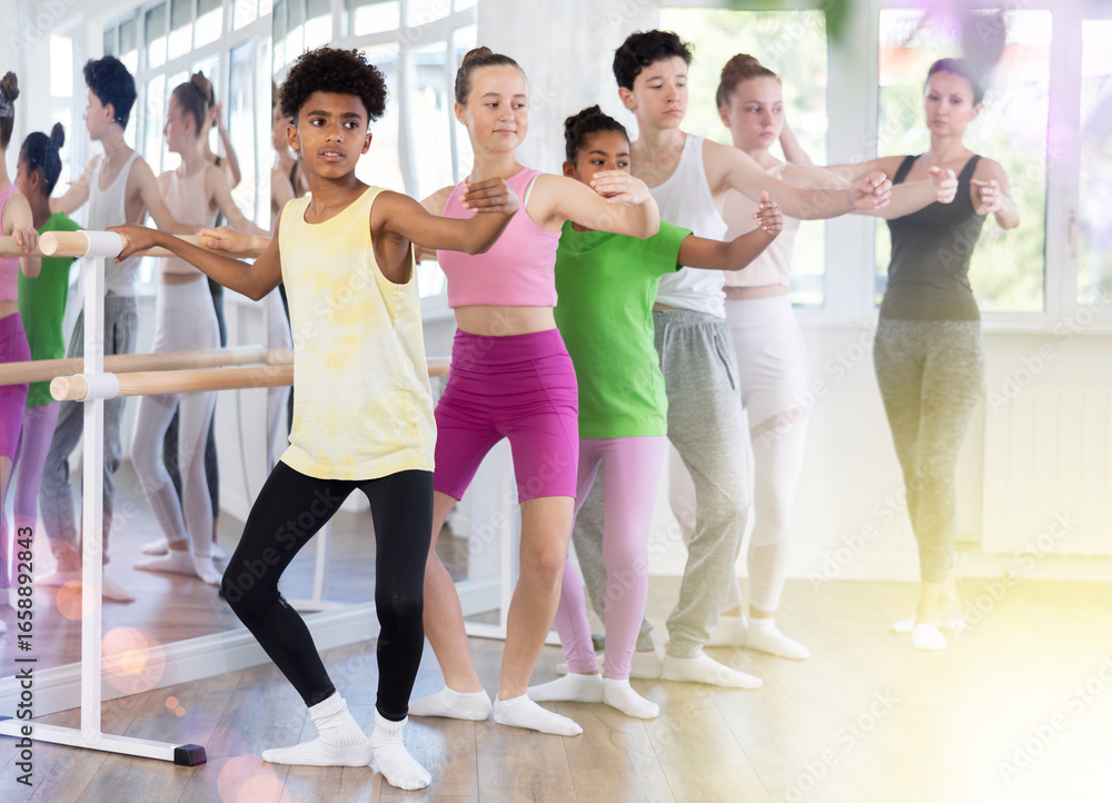 Fototapeta premium Adult woman teacher corrects plie movement of teenage boys and girls in studio