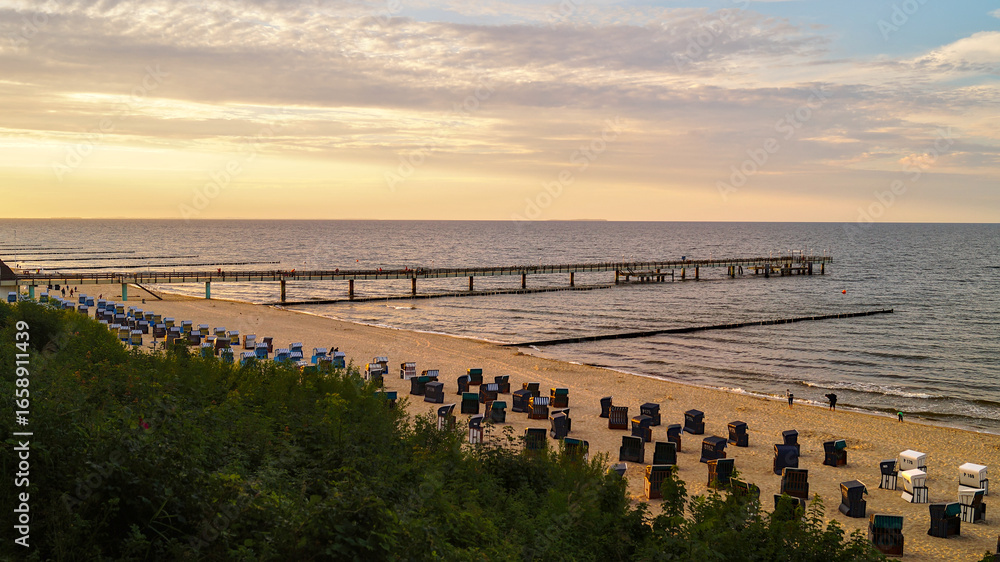 Obraz premium Koserow pier on Usedom with beach chairs on the sandy shore shortly before sunset – tranquil Baltic Sea seaside scene.