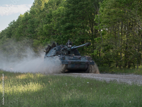 Принти на полотні Military tank advancing on dirt road through wooded area with dust trail