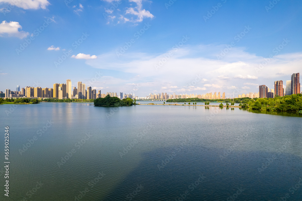 Obraz premium A wide lake reflects the sky near a city skyline with many tall buildings.