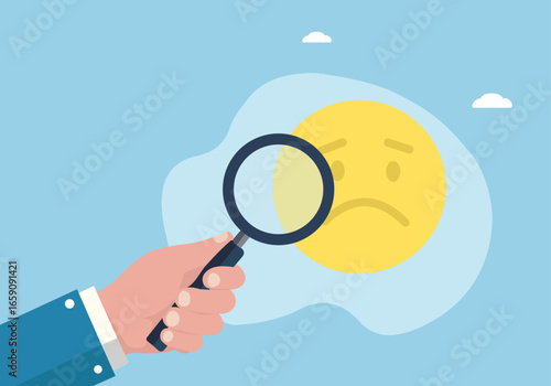 A hand with a magnifying glass inspects a sad face emoji, symbolizing the analysis of unhappiness, mental health, or focusing on negative feedback