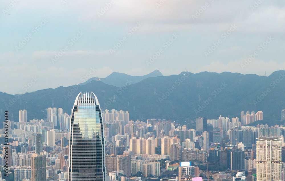Obraz premium Landscape of scenery aerial view on top of buildings in town Hong Kong. City with white cloudy by bright sunlight in with hotels and office towers with sunlight and mountain in morning is background.