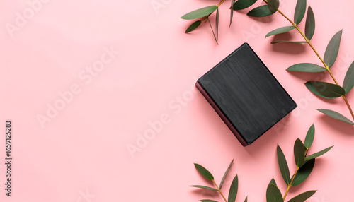 A handcrafted charcoal soap bar with green eucalyptus leaves on a pastel pink background with ample negative space