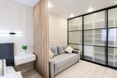 modern room features a gray sofa, a wooden slat divider, and a sliding door closet with frosted glass panels. Neutral colors create a calming space