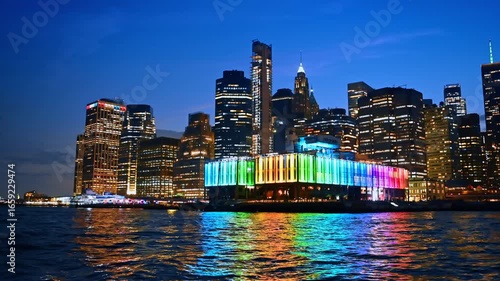 Rainbow illumination of the bar at pier 17 in New York, USA. View from a boat travelling by the river at night.