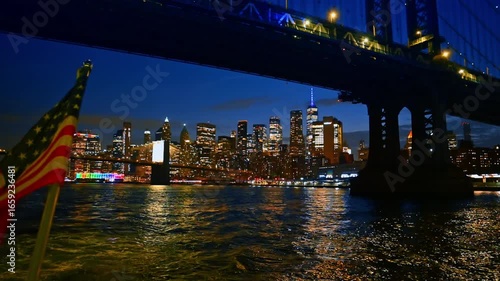 Boat travel by the East River under the Manhattan Bridge. Dazzling night skyline of New York at backdrop.