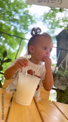 Little child blows bubbles in a milkshake with a straw. Summer family lifestyle moment with fun and joy