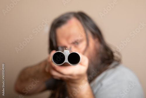 A man with a beard is holding a shotgun and pointing it at the camera