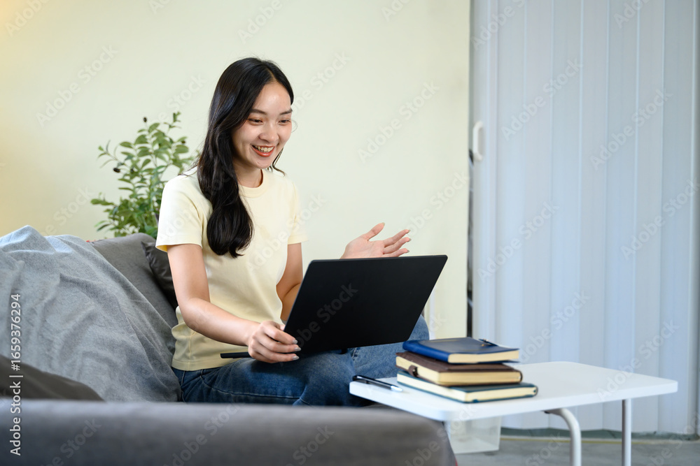 Young woman sitting on a sofa smiling while having an online video call using a laptop at home Young woman sitting on a sofa smiling while having an online video call using a laptop at home